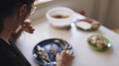 Mavi bir tabakta balık kemiklerini etten ayıran genç bir kadının omzunun üstünden.