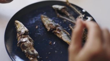 Dişi eller, yemeden önce pişmiş sardalyaların kemiklerini lacivert bir tabakta fileto yapıp çıkarıyor.
