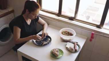 Pencerenin yanındaki masada oturan genç bir kadın elleriyle ızgara balığın kemiklerini çıkarıyor.