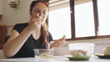 Bardaklı kadın sağlıklı bir salatanın ve pencerenin yanındaki masada tam buğday ekmeğinin tadını çıkarıyor.