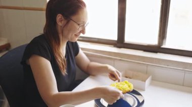 Gülümseyen kadın gözlüklü sarı safranlı risottoyu paket kutusundan mavi bir tabağa koyuyor.