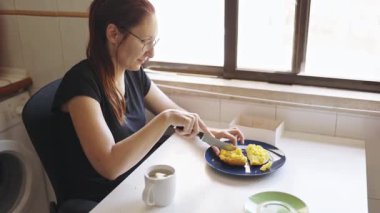 Mutfakta bir kadın sabah yemeği sırasında tabakta bıçakla sarı bir pasta kesiyor.