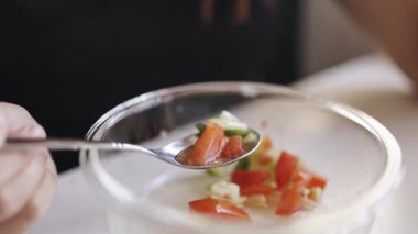 Gözlüklü genç bir kadının cam kaseden kaşıkla sağlıklı sebze salatası yemesi.