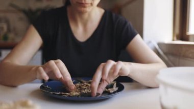 Kafkas kadın mutfakta bir masada oturuyor, elleriyle ızgara balık yiyor.