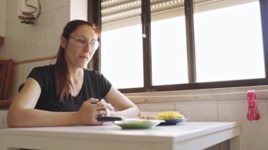 Gözlüklü neşeli genç bir kadın kahvaltısı kameraya gülümsüyor.