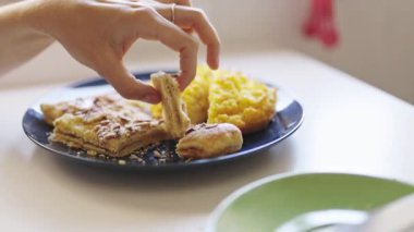 Gözlüklü genç bir kadın kahvaltıda tabaktan tatlı bir pasta yiyor.