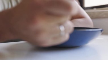 Uzun saçlı, sakallı, sabah yemeği yiyen ve pencereden dışarı dikkatlice bakan bir adamın yakın çekimi.