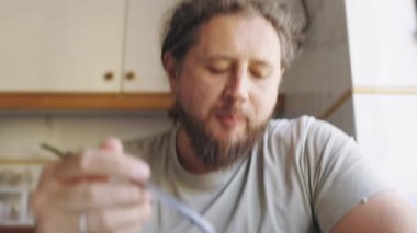 Sakallı, orta yaşlı bir adam mutfaktaki mavi kaseden taze sebze salatası yiyor.