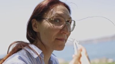 Deniz kenarında güneşli bir günde dışarıda soğan yiyen gözlüklü komik olgun kadın.