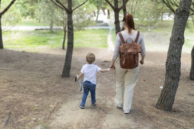 Anne ve oğlu, doğanın güzelliği arasında sevgi dolu anılar yaratırken elleri birbirine kenetlenmiş, sakin bir ormanda sakin bir şekilde gezintiye çıkıyorlar.