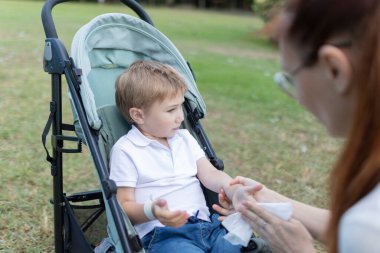 Annesi elindeki yarayı temizlerken küçük çocuk bebek arabasında oturuyor.