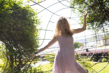 Yeşil yapraklarla çevrili açık pembe bir elbiseyle zarif bir şekilde hareket eden genç bir kadın.