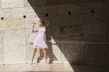 Pembe bir elbiseyle zarif bir dans sergileyen bir kadın dokulu taş bir duvara karşı.