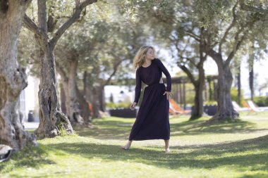 Yaşlı zeytin ağaçlarıyla güneşli bir bahçede modern dans eden bir kadın.