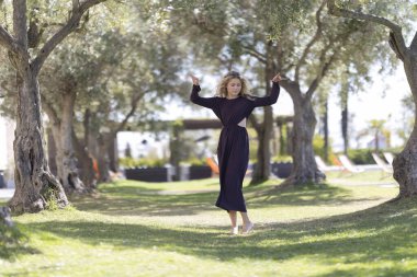 Eski zeytin ağaçları arasında zarif bir şekilde yürürken neşe ve özgürlüğü ifade eden bir kadın.