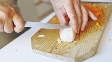 Aşçı ellerinin, rendelenmiş havuç ve soyulmuş patatesin yanında ahşap kesme tahtasıyla soğan doğramasını kapat.