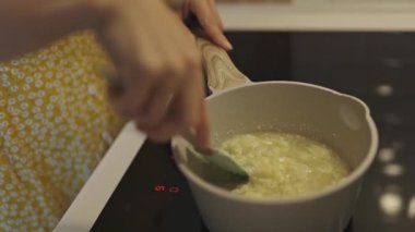 Bir tencerede erimiş tereyağı ve doğranmış sarımsak karıştıran kadın ellerini yakın.