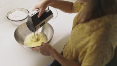 Fırıncının paslanmaz çelik bir kasede elektrikli mikserle yumurta çırptığı mutfak sahnesi.