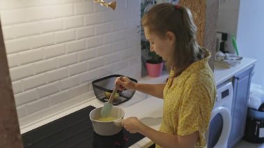 Sarı elbiseli bir kadın, yemek pişiriyor ve yemek karıştırıyor.