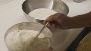 Tanınmayan kişi hamur hazırlıyor, hamur pişirmek için sıvıyla bir kaba un ekliyor.