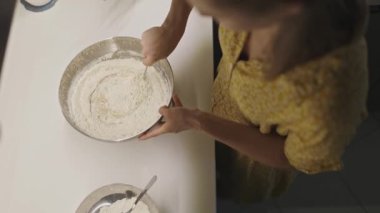 Yüksek açılı bir kadın fırıncı hamur pişirmek için kaşıkla malzemeleri karıştırıyor.