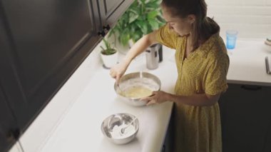 Metal bir kasede hamur hazırlayan ve malzemeleri karıştıran genç bir kadının yüksek açılı görüntüsü.