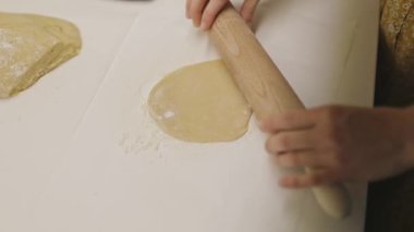 Beyaz unlu bir yüzey üzerinde ahşap bir iğneyle hamuru yuvarlayan dişi fırıncı.