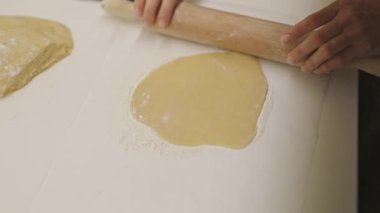 Dişi fırıncı beyaz bir yüzey üzerinde ahşap bir raptiyeyle hamur işi yapıyor.