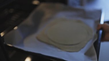 Ham hamurla pişirme tepsisini sıcak fırına koyan bir insanın ellerini kapatın.