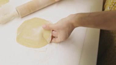 Dişi fırıncı elleri, un kaplı bir yüzeyde taze hamuru yassılaştırmak için ahşap bir merdane kullanıyor.