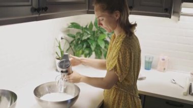 Genç bir kadın, tatlı hazırlarken paslanmaz çelik bir kasede el çırpıcısı ile krema çırpıyor.