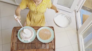 Bir pasta şefinin parlak, modern bir mutfakta pastaya beyaz krema sürüşü.