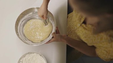 Bir kadının elleri, kek hamuru ya da ekmek hamurunu metal bir kaseye karıştırırken tepeden aşağı bakıyor.