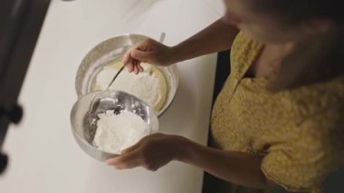 Metal bir kâseye un ekleyip kaşıkla karıştırarak hamur hazırlayan kadın.