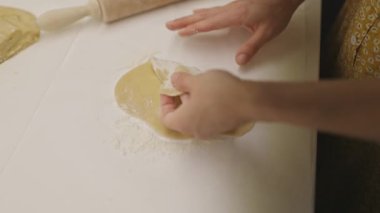 Kadınların elleri beyaz mutfak tezgahında hamuru dikkatlice katlar ve un ile hazırlar.