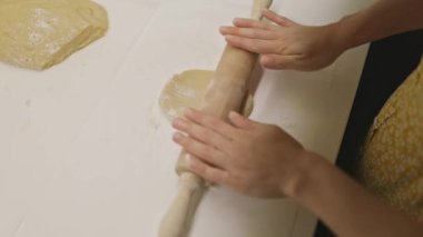 Bir kadının elleri, ahşap bir okla hamuru düzleştirirken yüksek açılı görüntüsü.