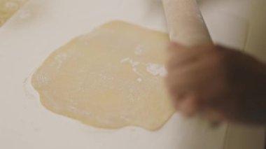 Aşçı ahşap bir oklava kullanarak beyaz bir yüzey üzerinde taze hamur düzleştiriyor.