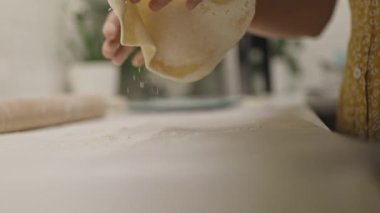 Kadın elleri, un kaplı mutfak tezgahında ağır çekimde makarna hamuru hazırlıyor.