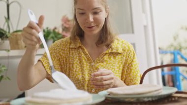 Beyaz kadın mutfak masasında ev yapımı kreplere beyaz krema sürüyor.