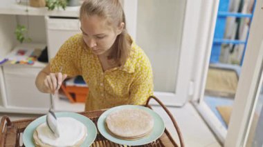 Genç bir kadın evde lezzetli bir ballı pasta hazırlarken katmanlar arasında kremalı dolgu yapıyor.