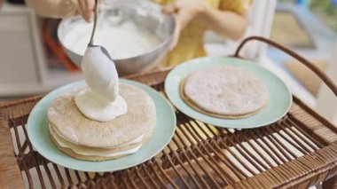 Şekerci lezzetli bir tatlı yapmak için sünger kekine beyaz krema sürüyor.