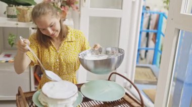 Neşeli bir şekilde gülümseyen genç bir kadın sıcak, güneşli bir mutfakta lezzetli bir ev yapımı tatlı hazırlıyor.