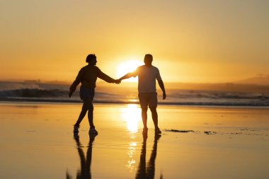 Romantik çift gün batımında okyanus sahilinde el ele yürürken yaz tatilinin tadını çıkarıyor.