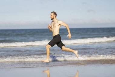 Man running barefoot along the shoreline, getting exercise during a sunny beach vacation