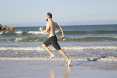 Young man running barefoot on a sunlit beach, enjoying fitness and an active summer lifestyle