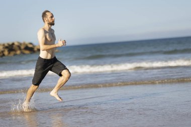 Man running barefoot along the ocean shoreline, splashing water and staying fit