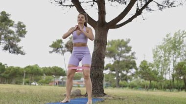 Sporty young woman doing squats and side leg raises with a resistance band in a park