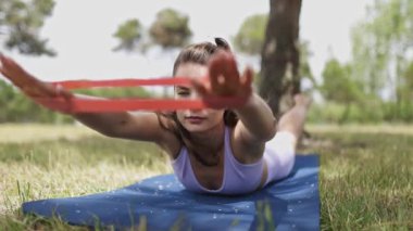 Fit young woman strengthening her back and arms using an elastic band while lying on a yoga mat