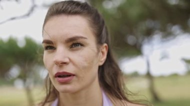 Young athletic woman breathing heavily and flexing her muscles in a park after training