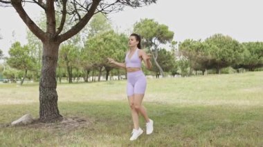 Fit young woman doing cardio workout with a skipping rope on the grass in a beautiful public park